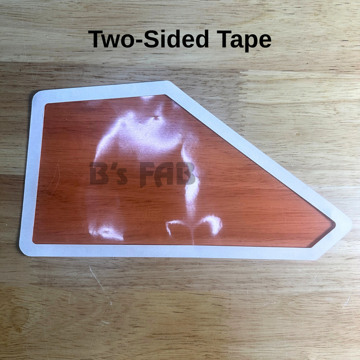 Orange irregular-shaped two-sided tape on wood surface.